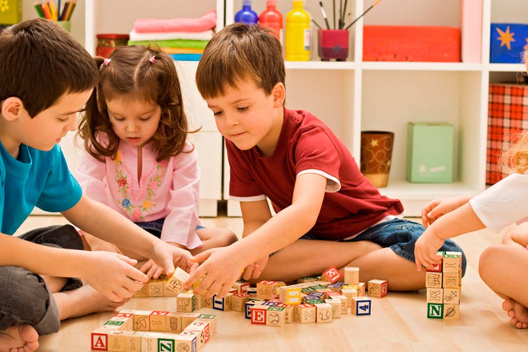  Three children are sitting on the floor and playing with wooden alphabet blocks.